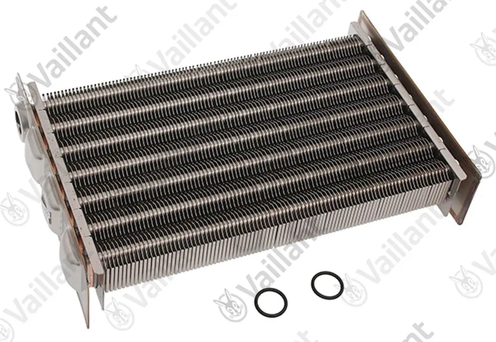 Vaillant Wärmetauscher mit mehreren Metallrippen und Anschlüssen, liegend auf einer Oberfläche, daneben zwei schwarze O-Ringe.